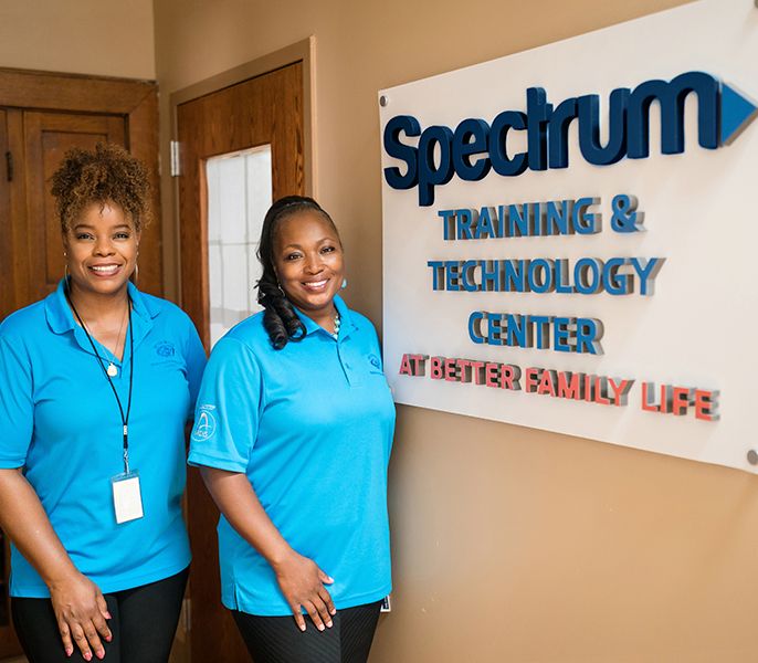 Spectrum Community Center Assist volunteers pose by a sign for Spectrum's new Training & Technology Center at A Better Family Life